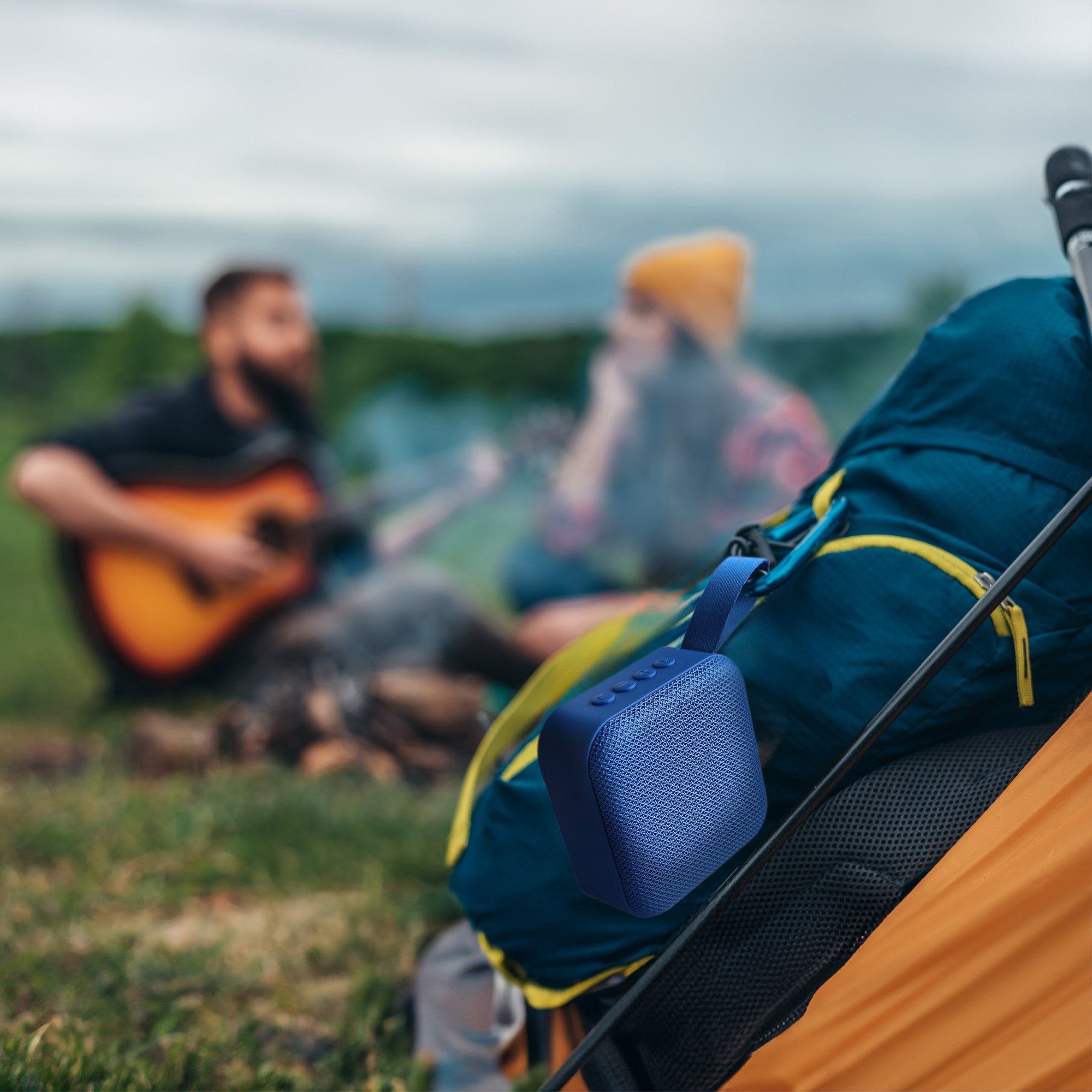 Blue portable wireless speaker clipped to tent strap, textured fabric body