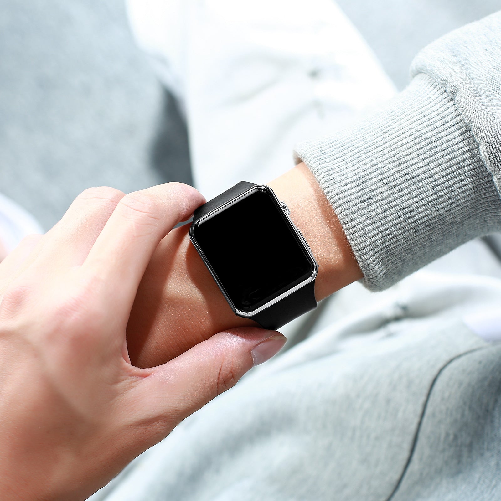 Digital electronic wristwatch on wrist, black screen, dark strap, brushed metal side.