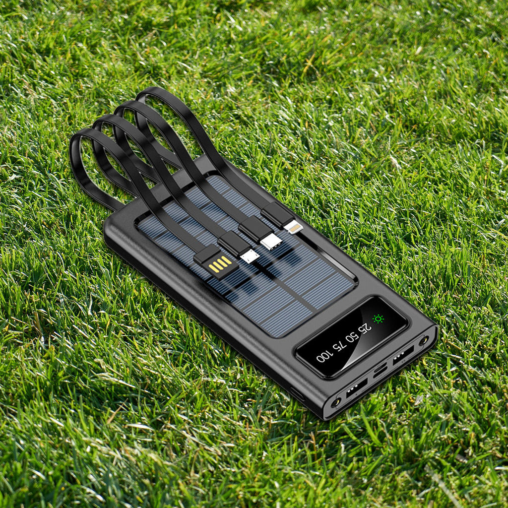 Black solar power bank with LED screen, USB ports, and charging cable on grass