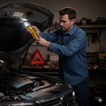Rechargeable yellow handheld flashlight with LED beam, used under vehicle hood.